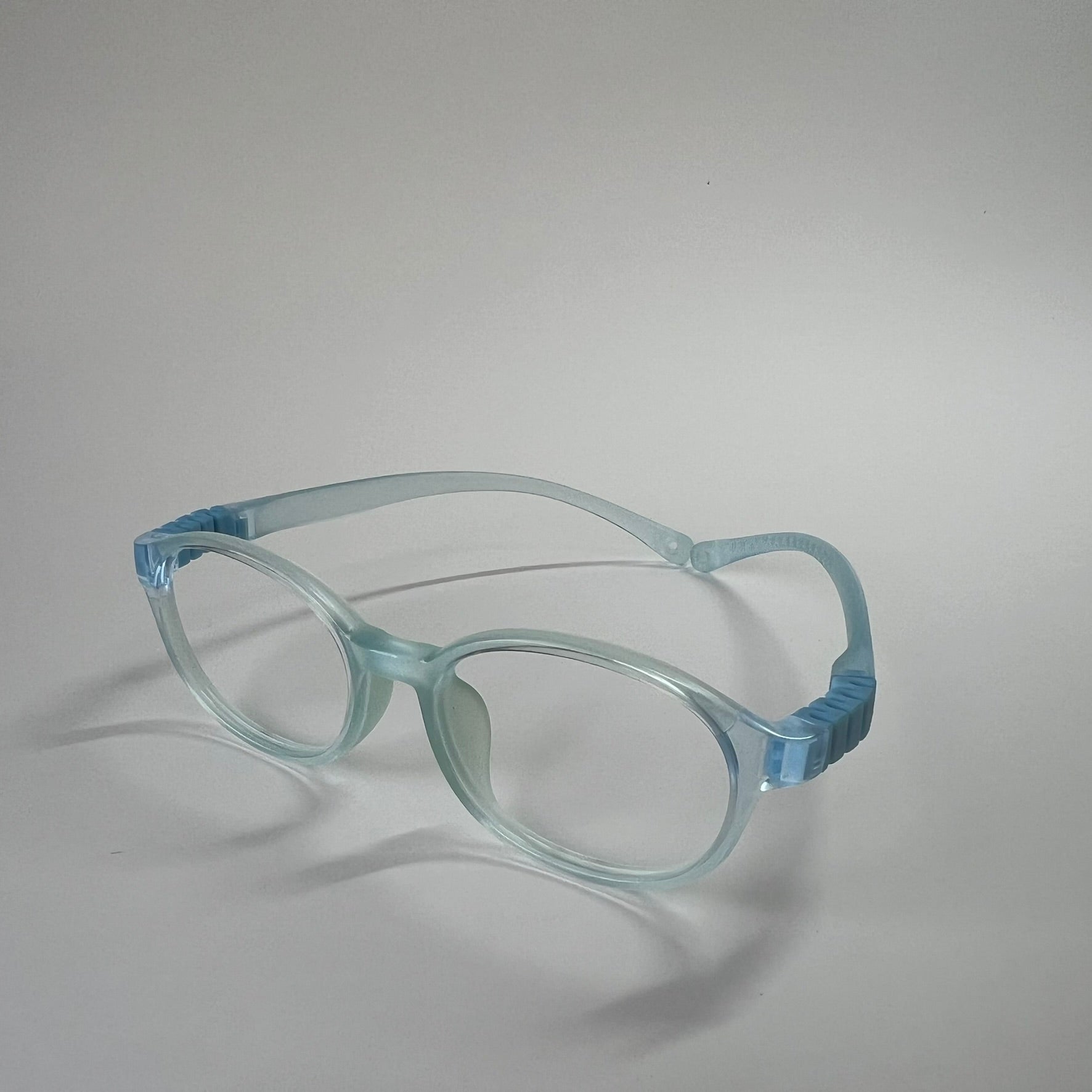 PureFlex kids flexible glasses in translucent jelly blue silicone material, showcasing the specialized wrap-around curved temple arms for ages 7-9. Side view.